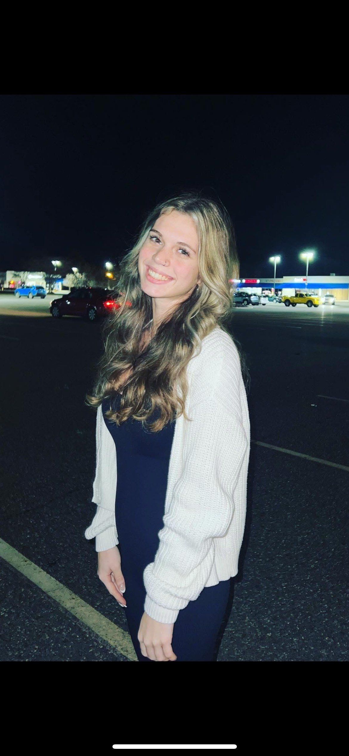 A woman is standing in a parking lot at night.