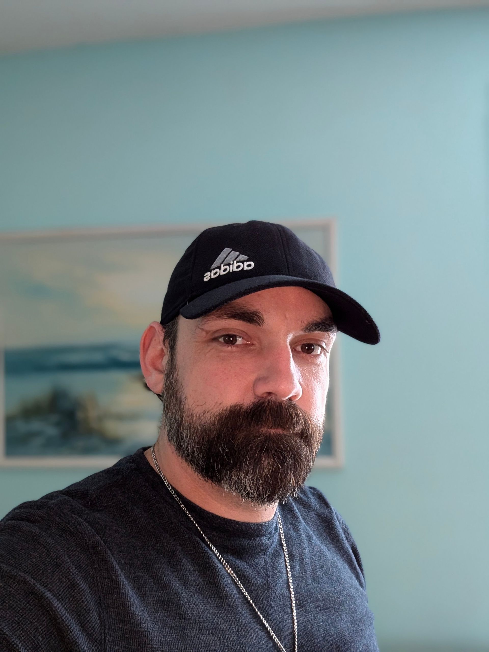 A man with a beard is wearing a black adidas hat.