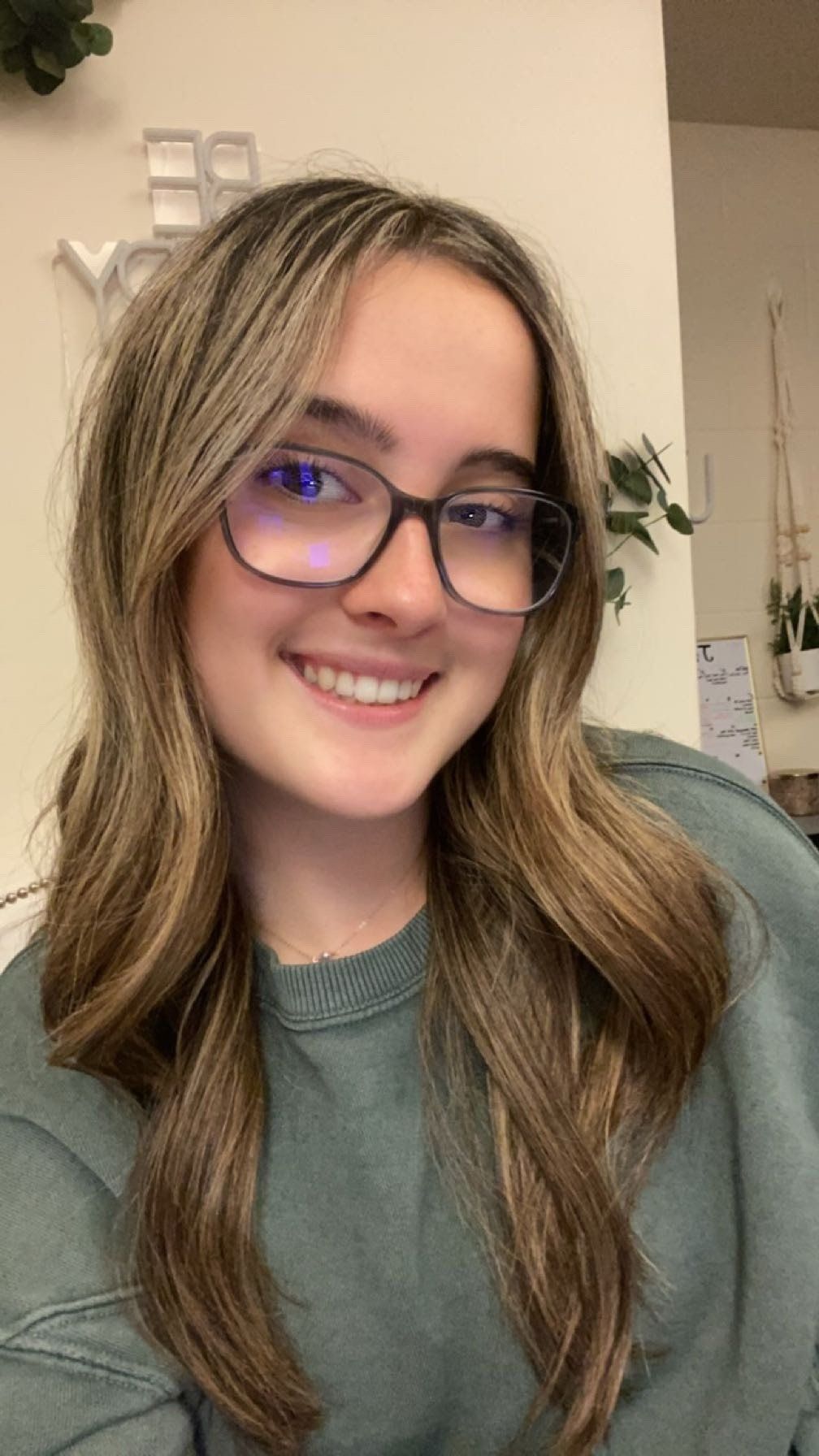 A young woman wearing glasses and a green sweater is smiling for the camera.
