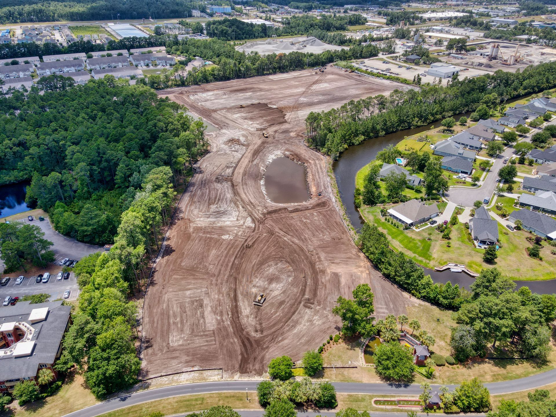 An aerial view of a construction site in a residential area surrounded by trees and a river.
