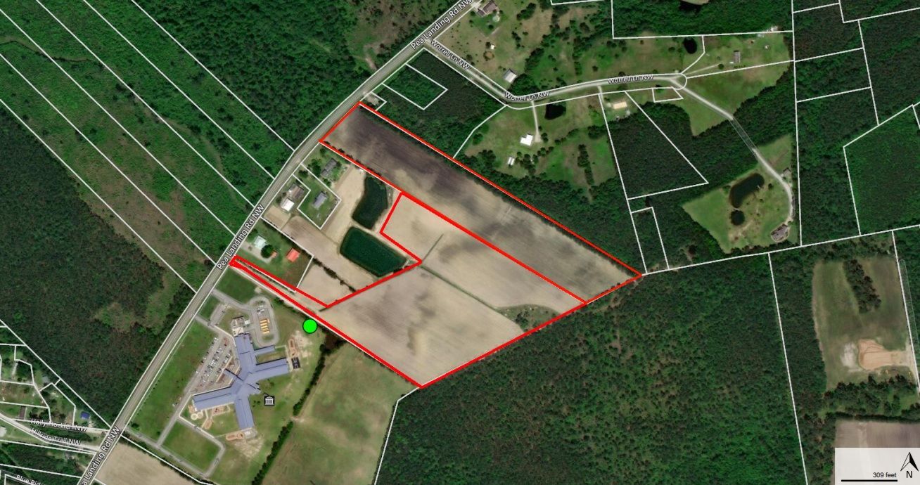 Aerial view of a plot of land outlined in red, showing a mix of cultivated fields and wooded areas.