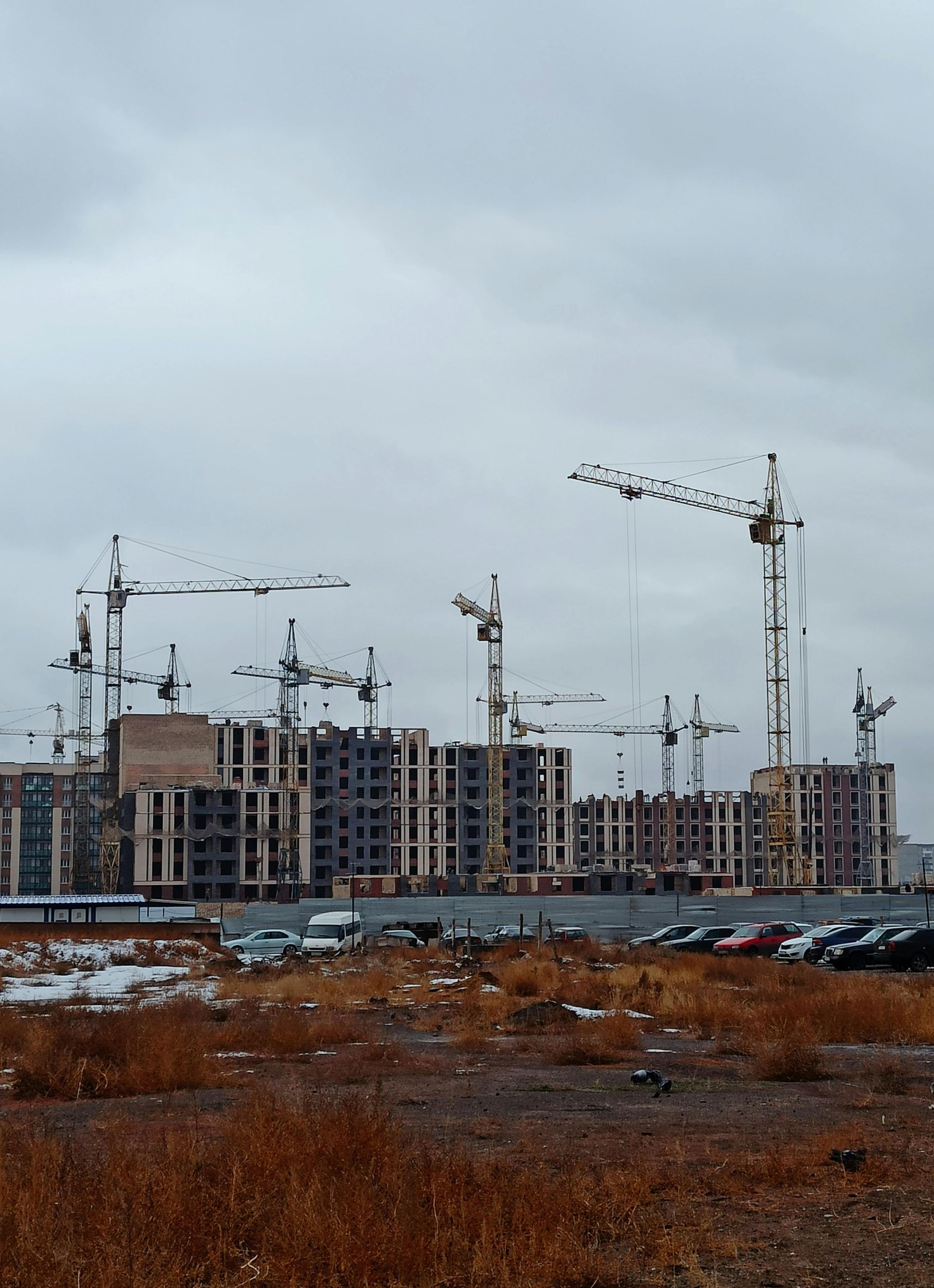 Construction site with several buildings under construction; many cranes under cloudy sky.