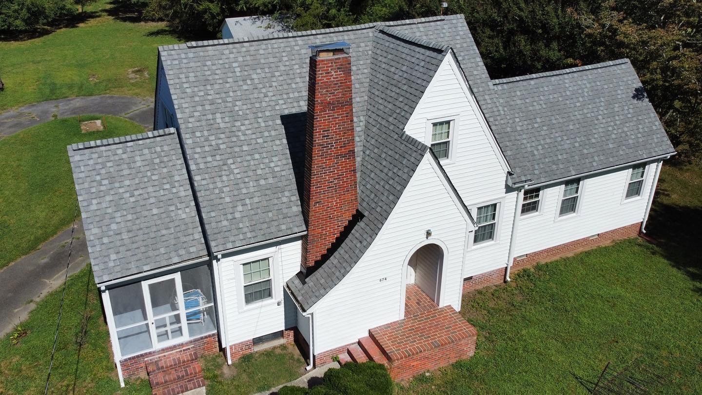An aerial view of a white house with a gray roof and a brick chimney.