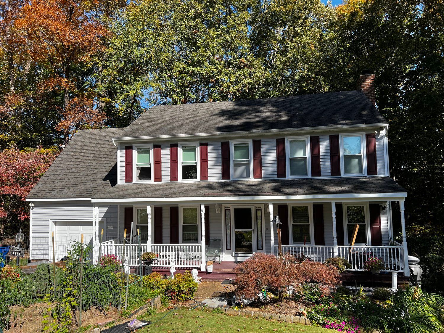 A large white house with a large porch is surrounded by trees.