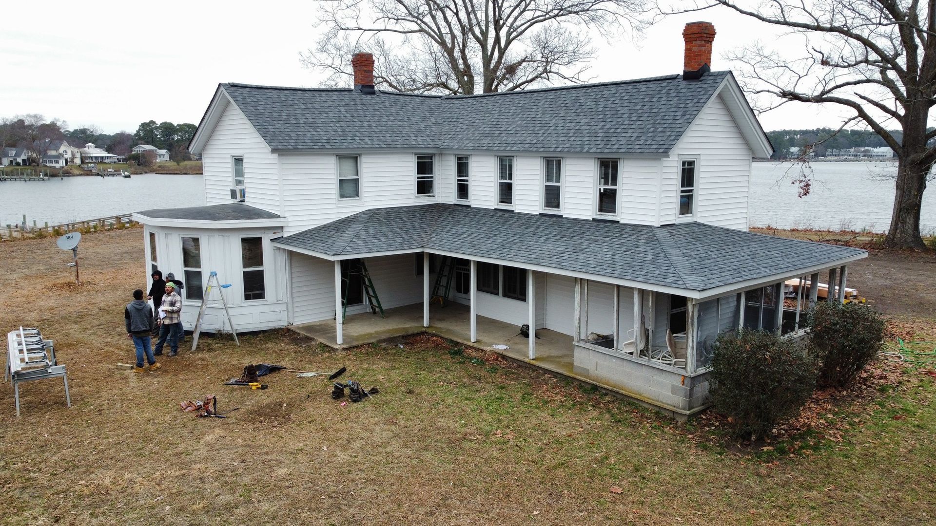 An aerial view of a large white house with a porch and a lake in the background.