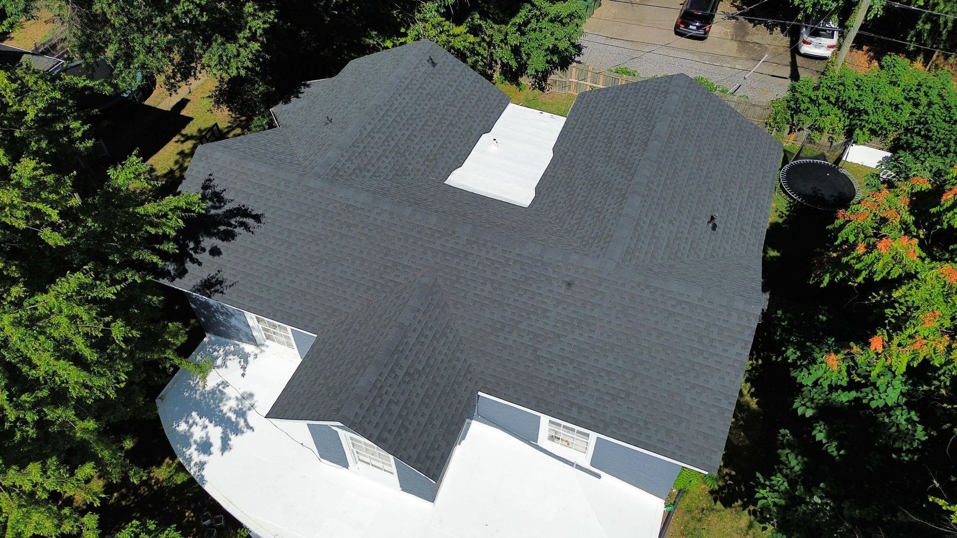 An aerial view of a house with a black roof surrounded by trees.
