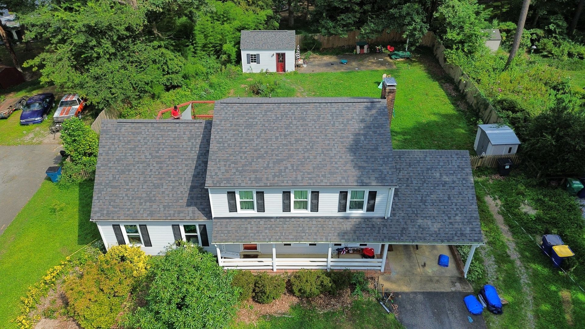 An aerial view of a house with a gray roof and a white house in the background.