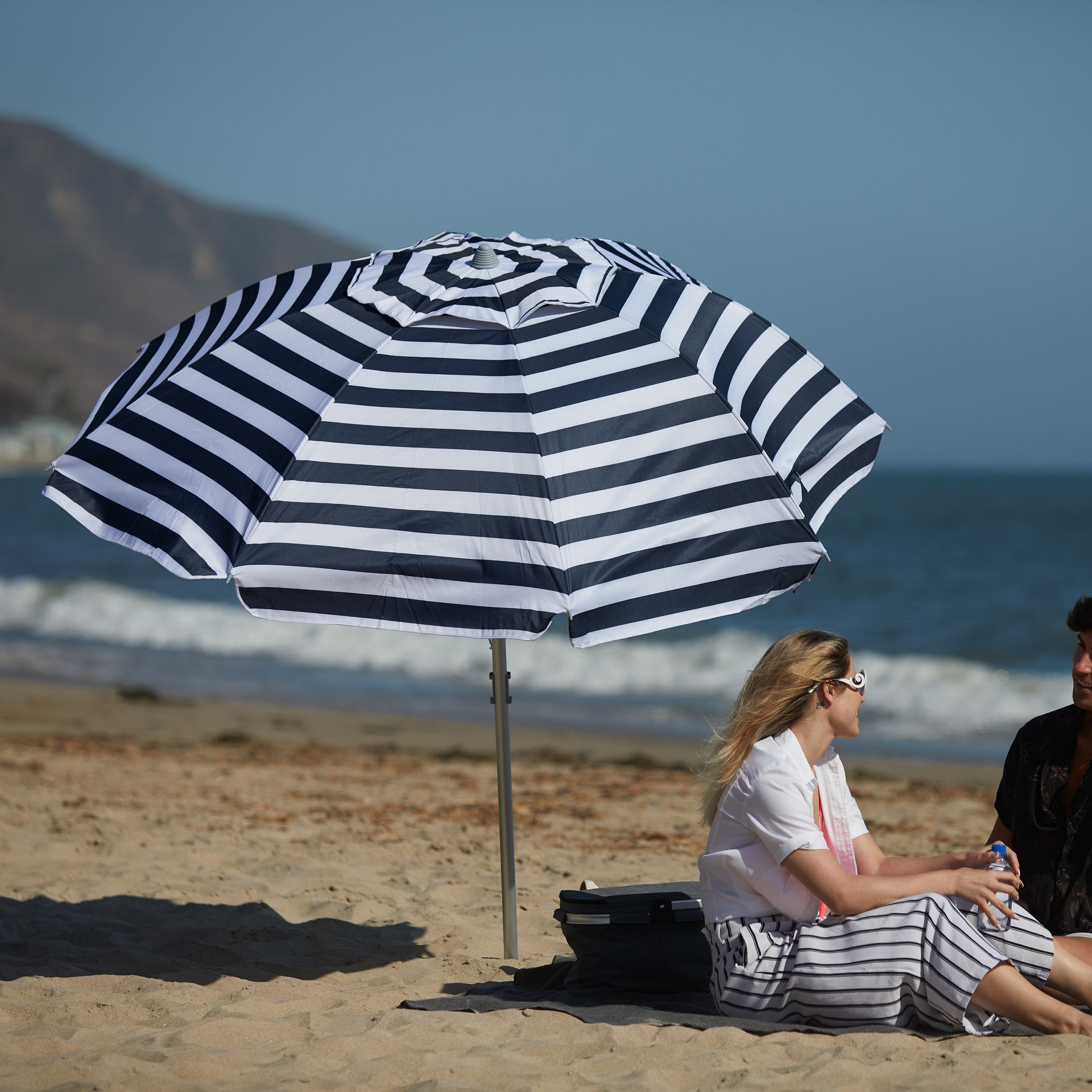A man and woman sit under an umbrella on the beach