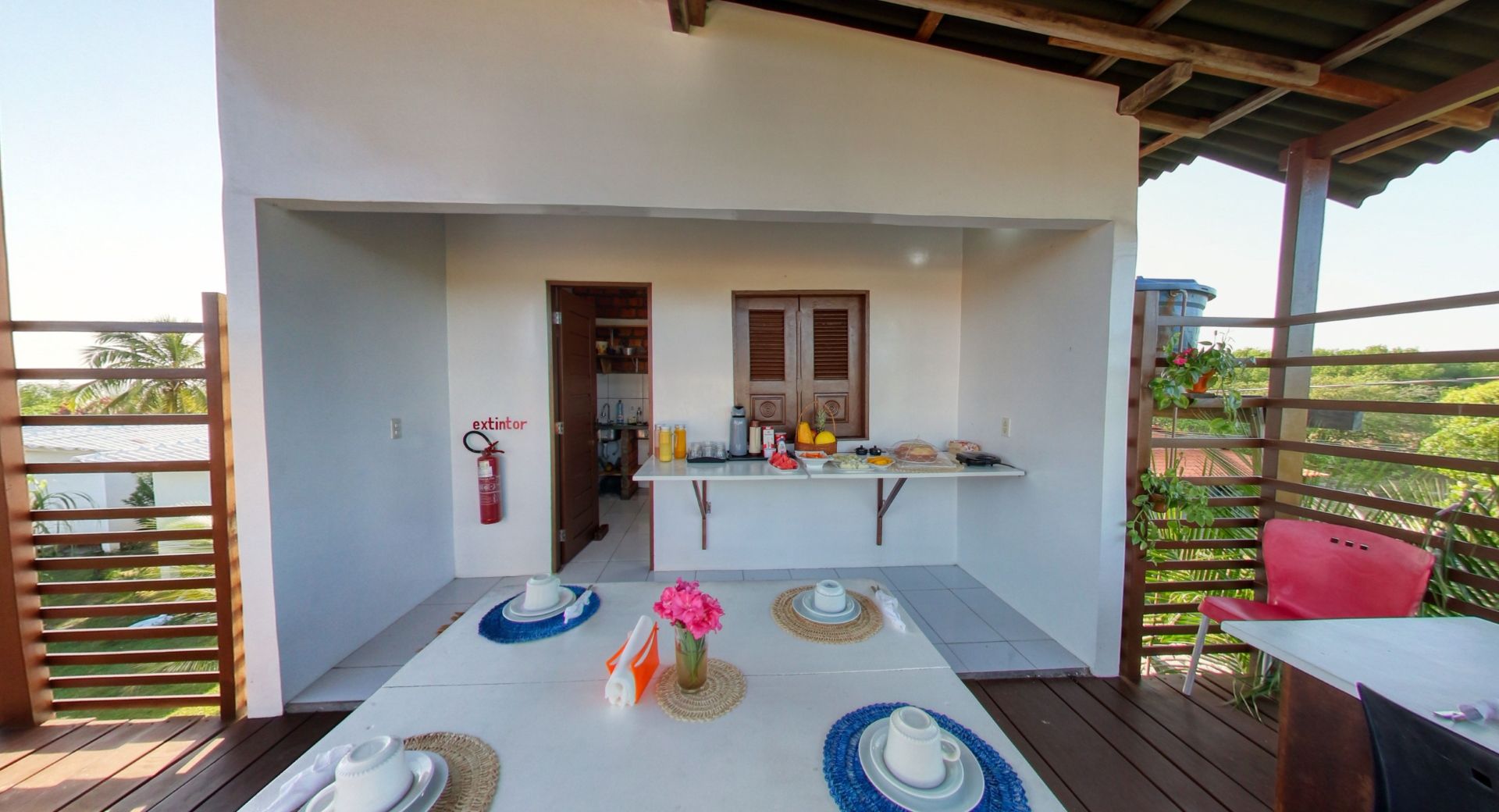 Área de jantar ao ar livre com mesa posta para café da manhã e exposição de alimentos.