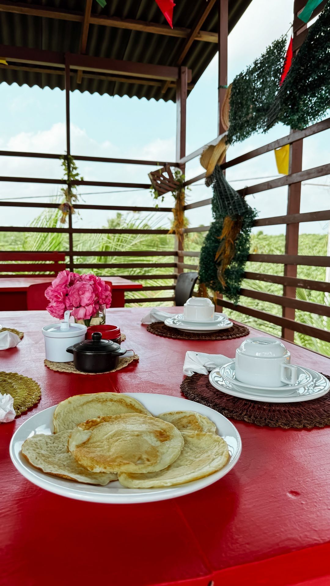Panquecas e chá em uma mesa vermelha, ao ar livre com vista para o campo.