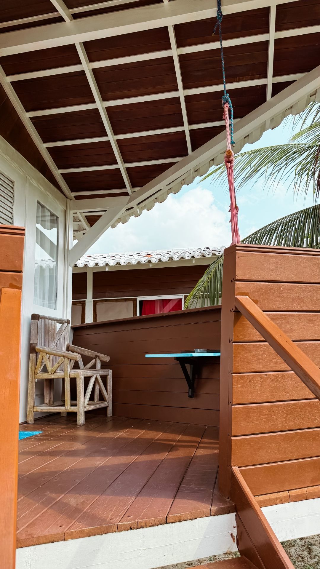 Varanda de madeira com balanço e assentos sob um telhado marrom e branco, céu azul.