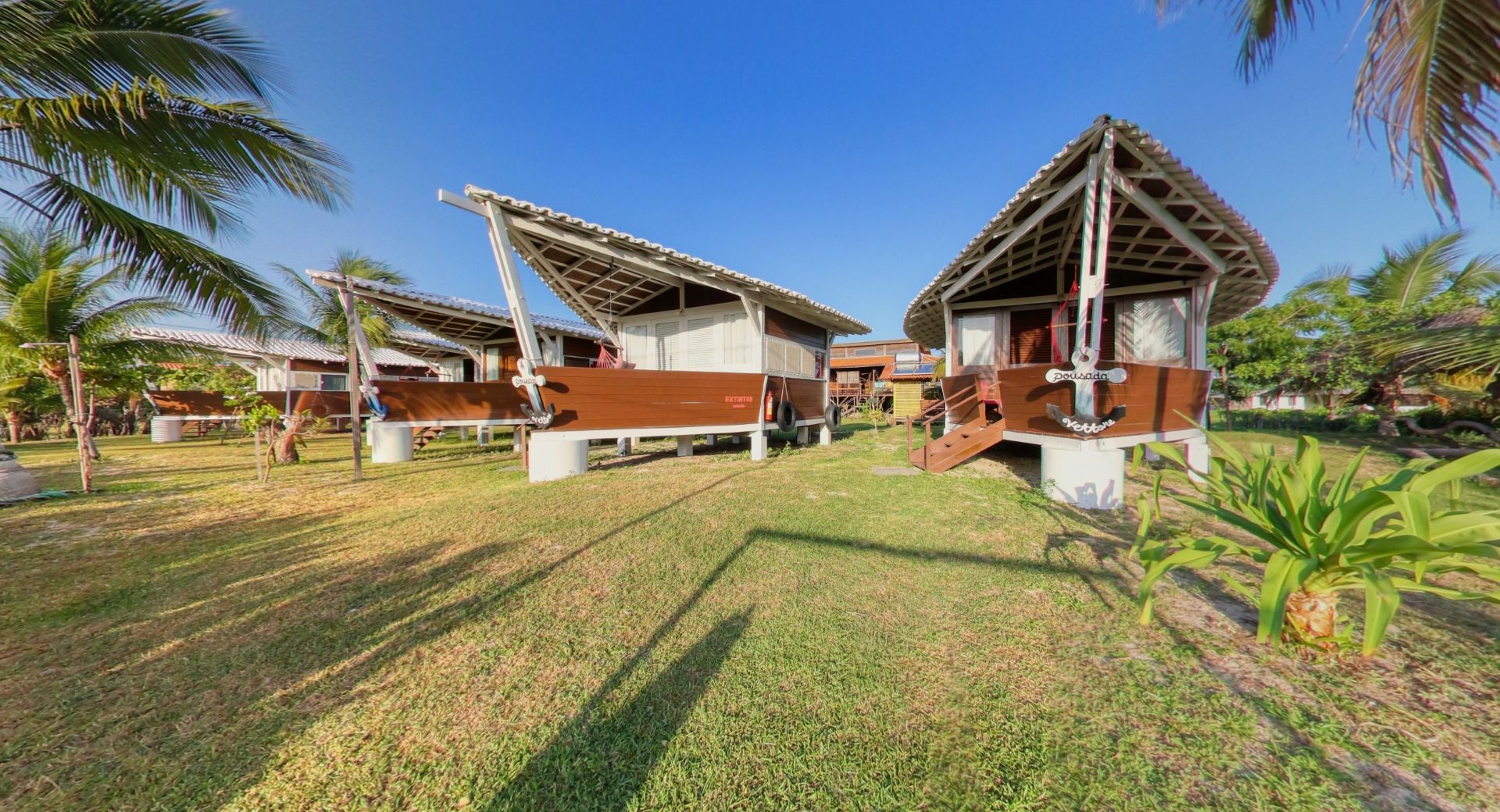 Bangalôs de madeira com telhados brancos e revestimento marrom em um gramado sob um céu azul.