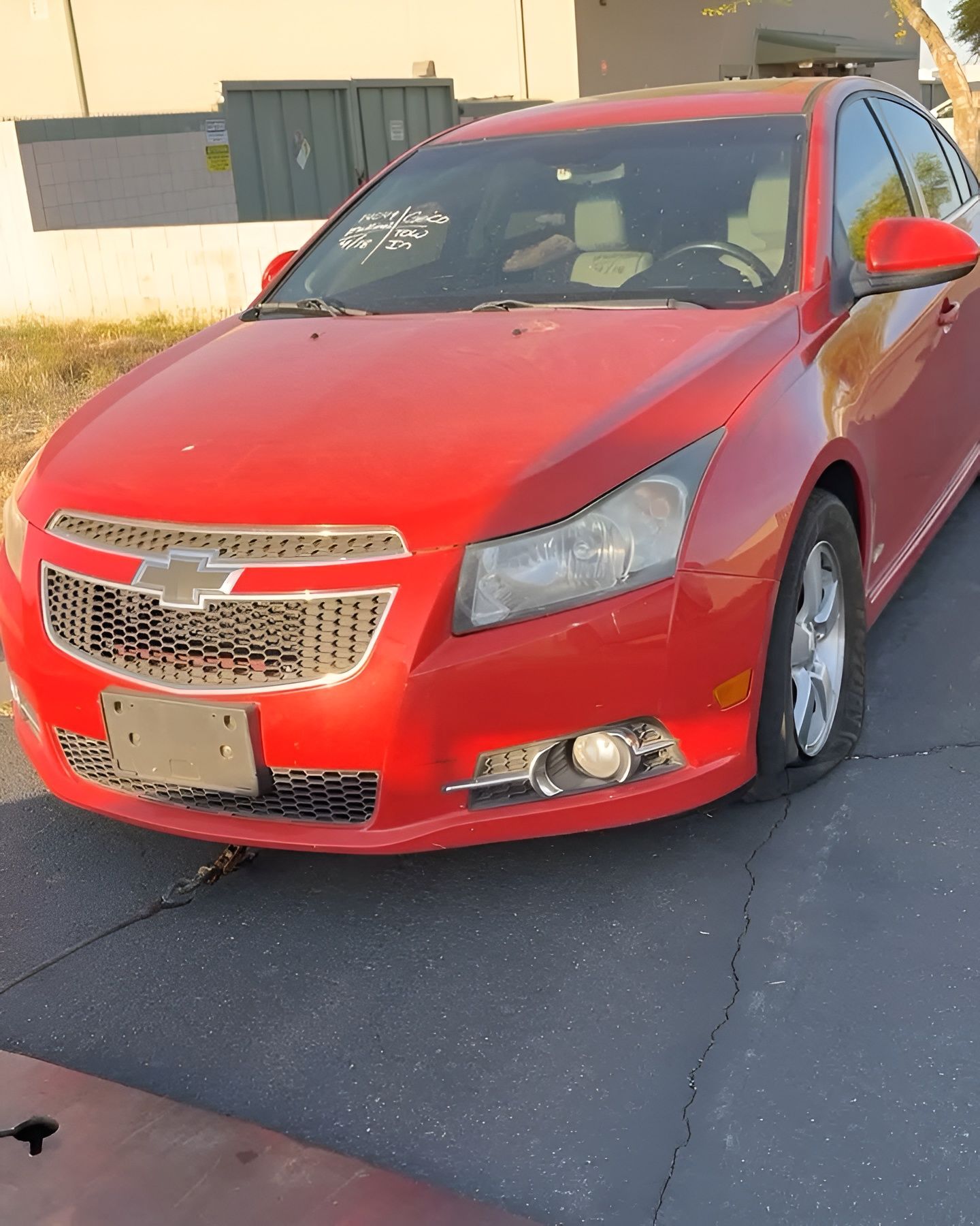 Red Chevrolet Cruze with a flat tire parked on asphalt. The car is facing the camera.