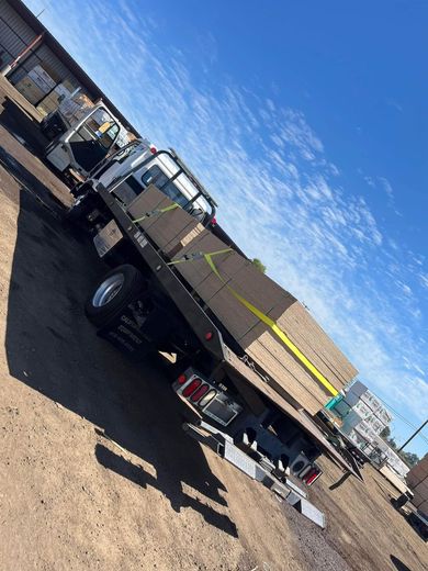 A flatbed truck loaded with lumber, secured with straps, parked outside under a blue sky.
