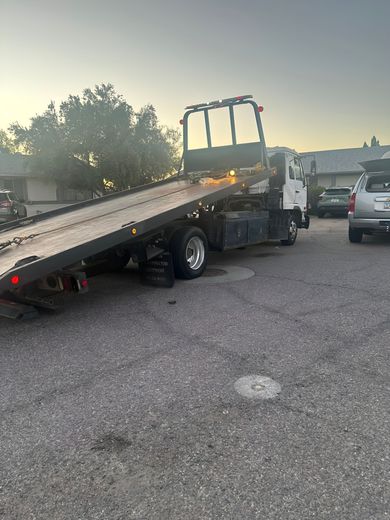 Tow truck on a gravel lot, the bed is extended, ready to load a vehicle. Dusk setting, the sky is pale.