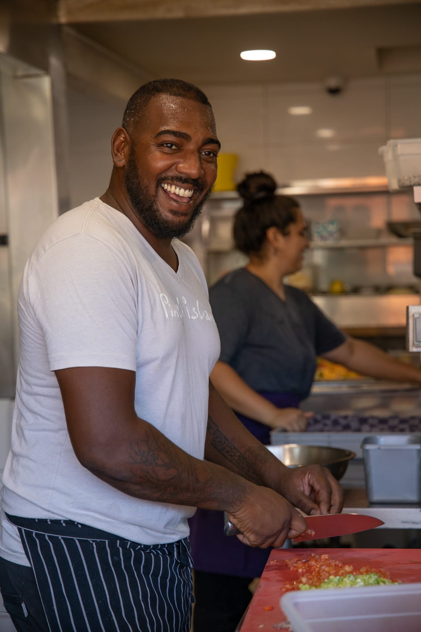 A man is smiling while cutting vegetables in a kitchen.