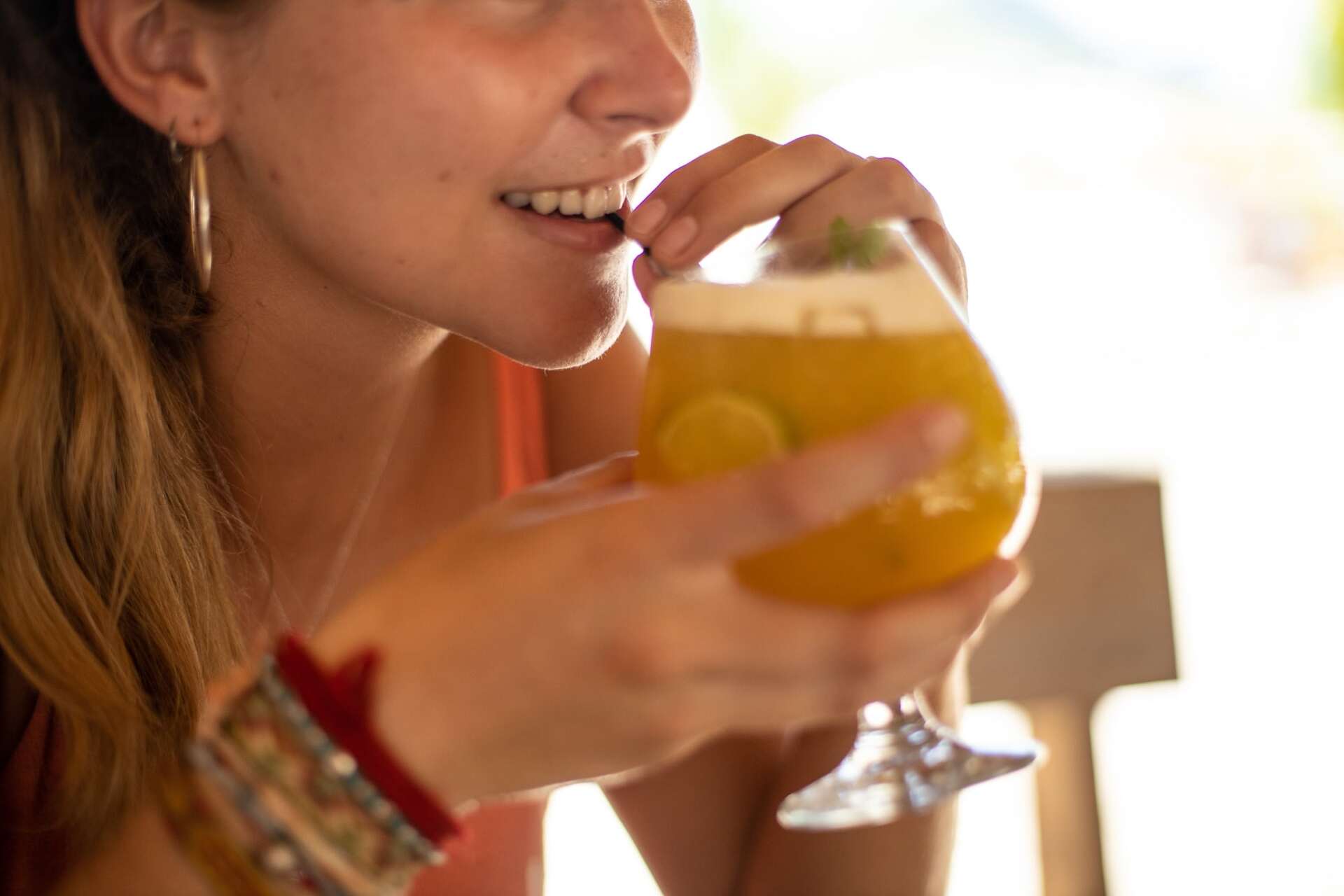 A woman is drinking a drink from a glass while sitting at a table.