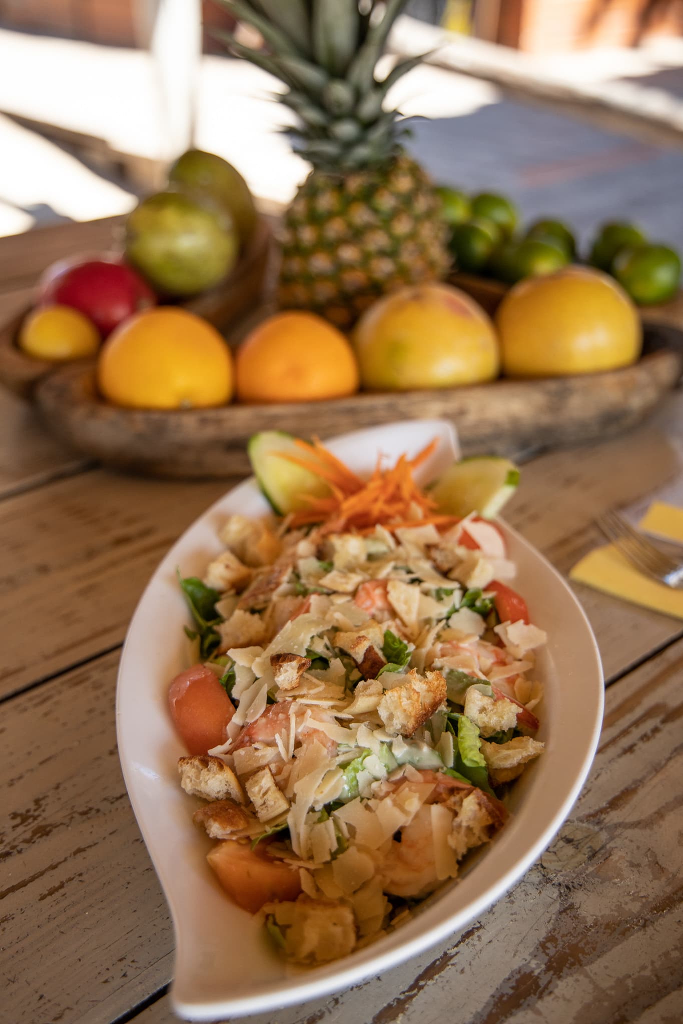 A bowl of food is on a table next to a bowl of fruit.