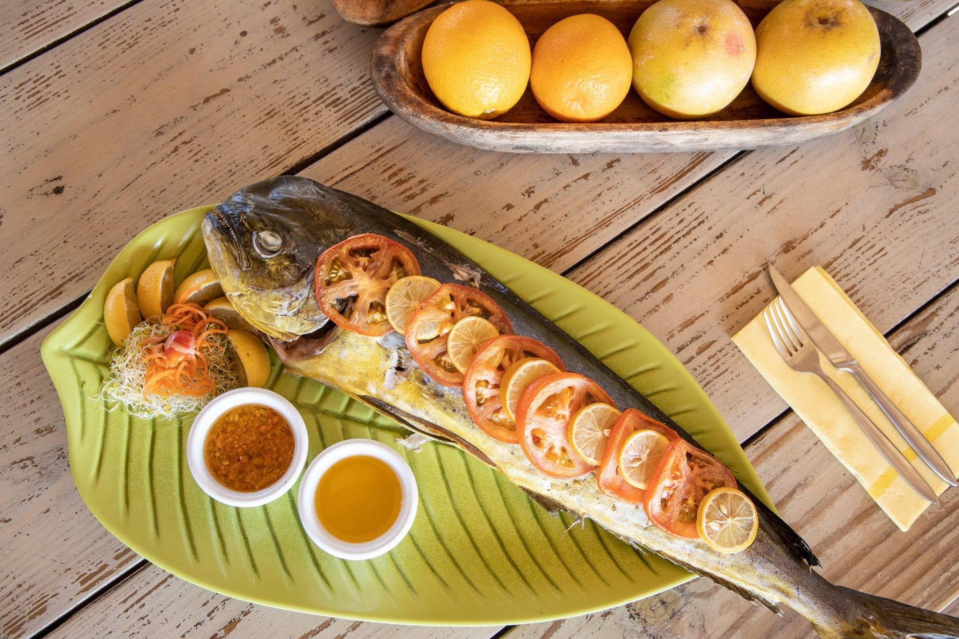 A large fish is sitting on a green plate on a wooden table.