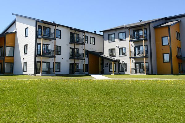 Immeubles d'appartements à deux étages avec balcons, extérieur gris et orange, pelouse verte, ciel bleu.