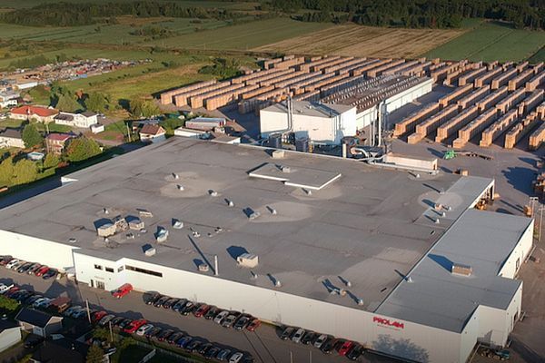Vue aérienne d'un grand bâtiment industriel avec des piles de bois et un stationnement.
