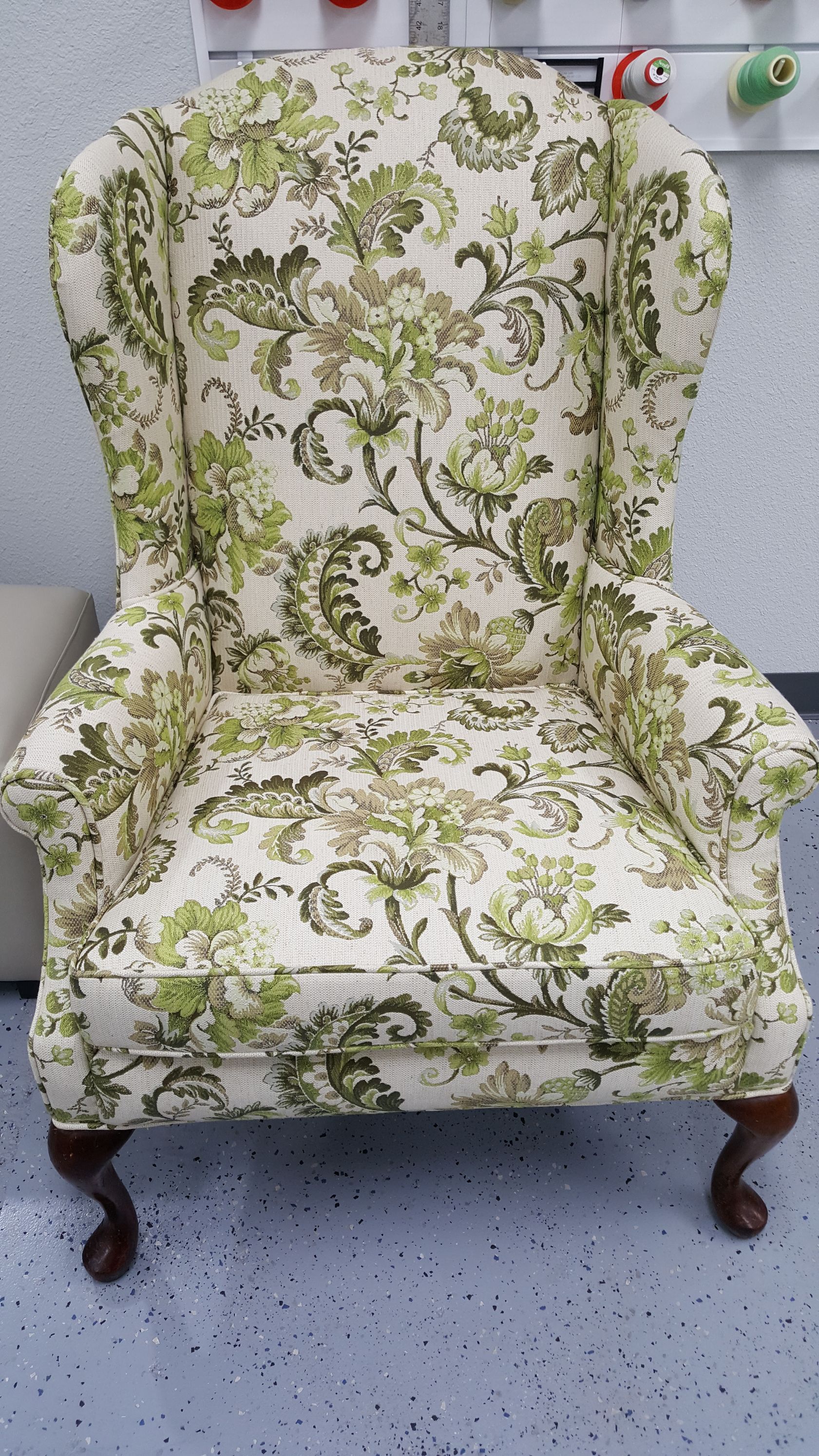 A green and white chair with a floral pattern is sitting on a tiled floor.