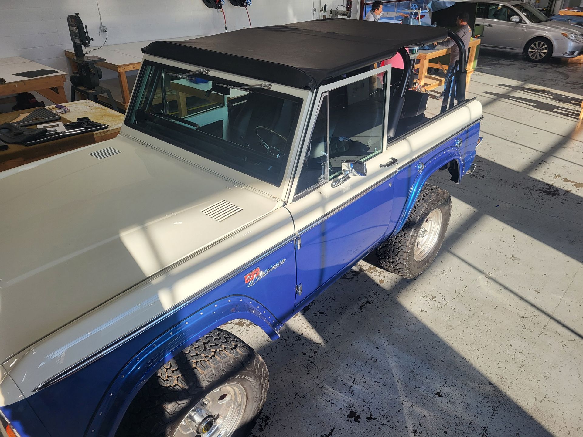 A blue and white jeep with a black top is parked in a garage.