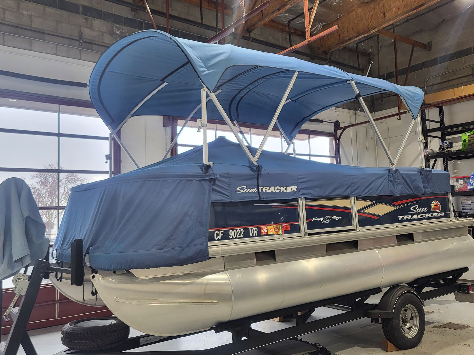 A pontoon boat with a blue canopy is sitting in a garage.