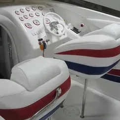 The interior of a boat with red , white and blue seats and a steering wheel.
