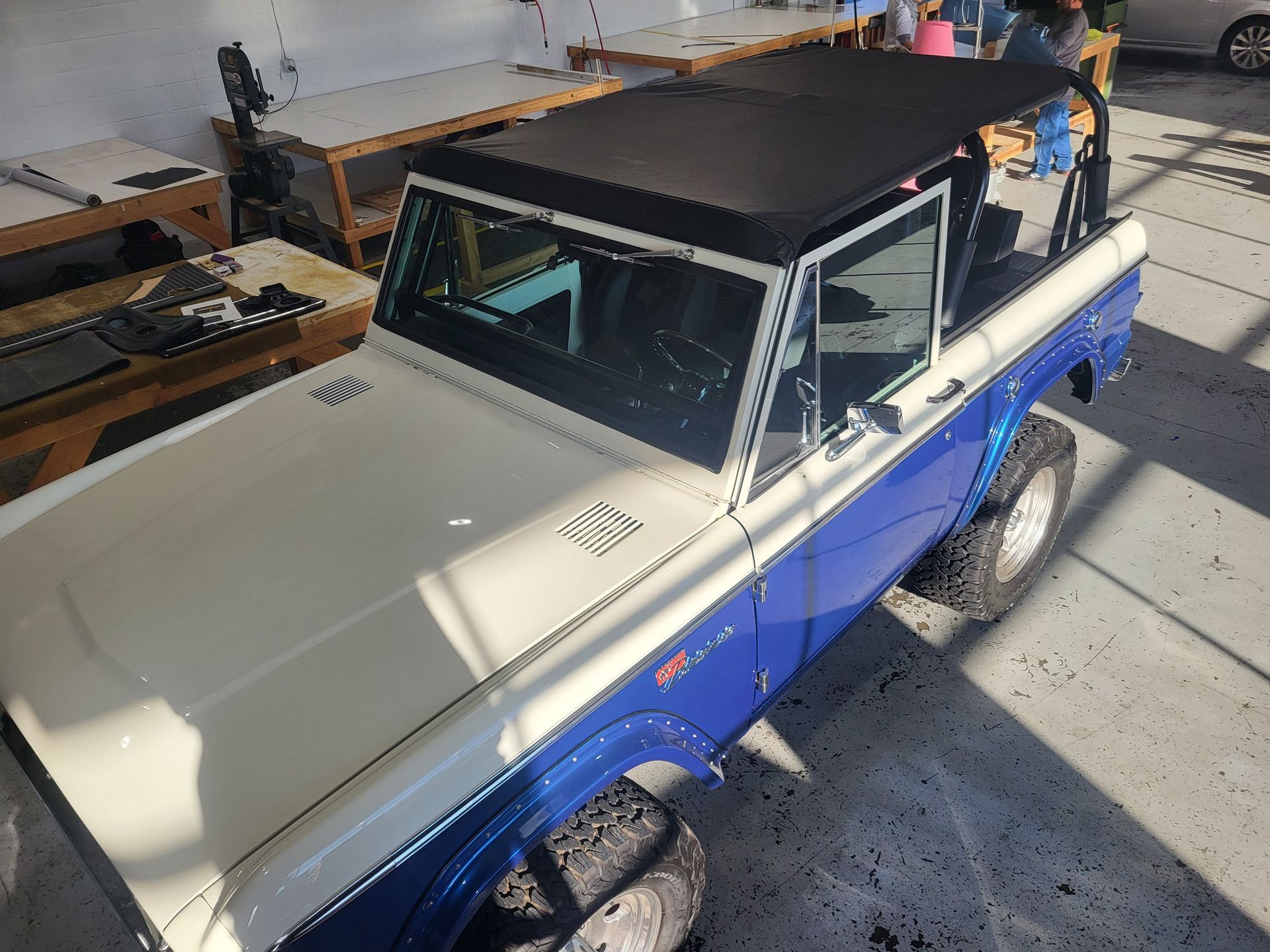 A blue and white truck with a black top is parked in a garage.