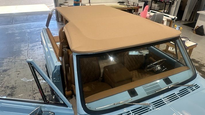 Light blue vintage SUV with a tan convertible top, open door. Brown interior.