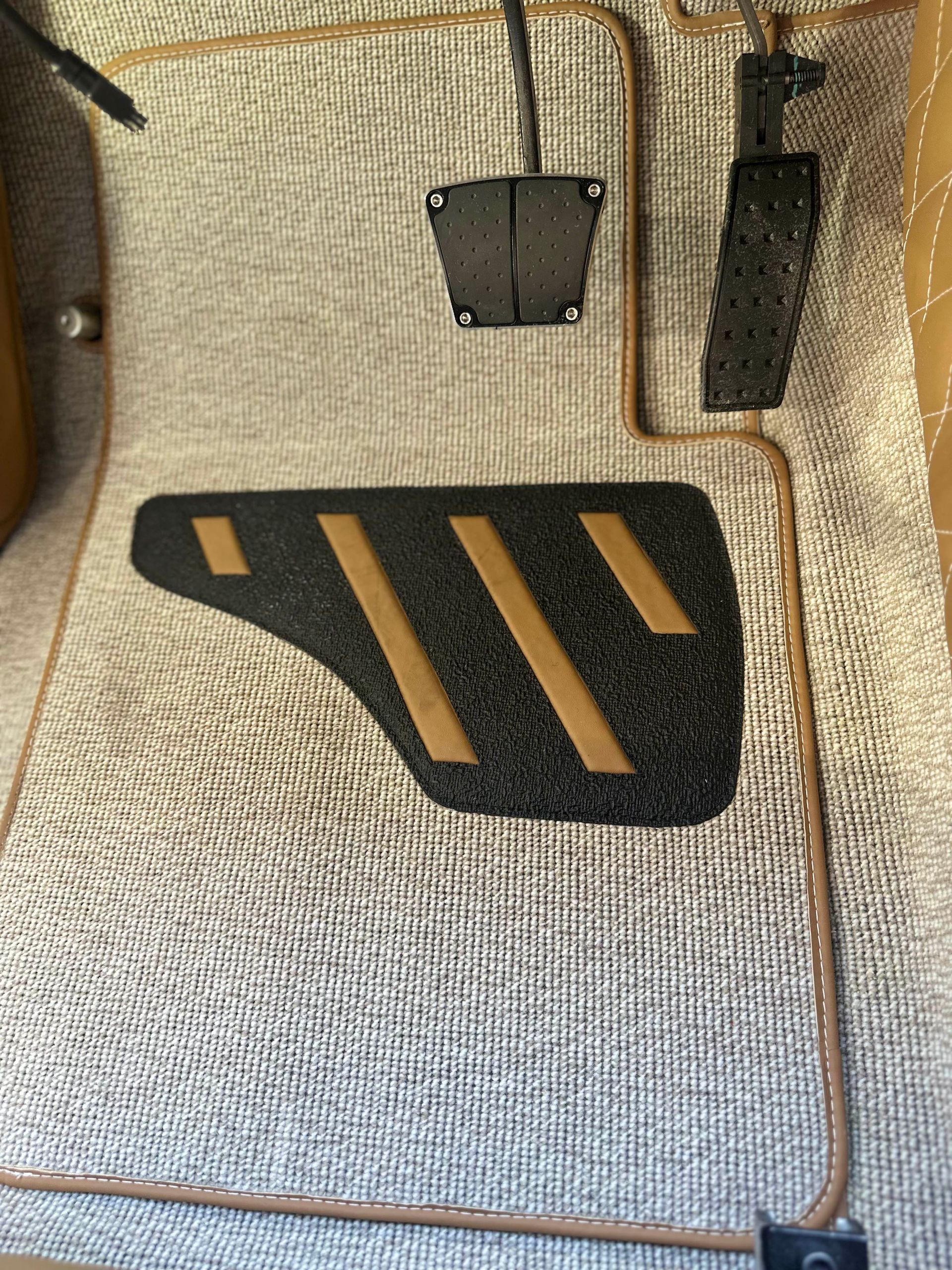 Car floor with metallic silver carpeting and black and tan pedals.