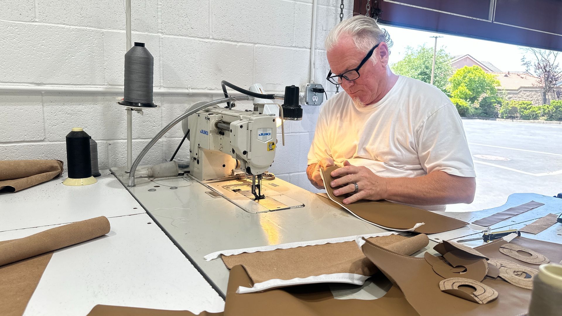 People working in a workshop; cutting, assembling materials. Interior shot, tools, equipment, and materials visible.