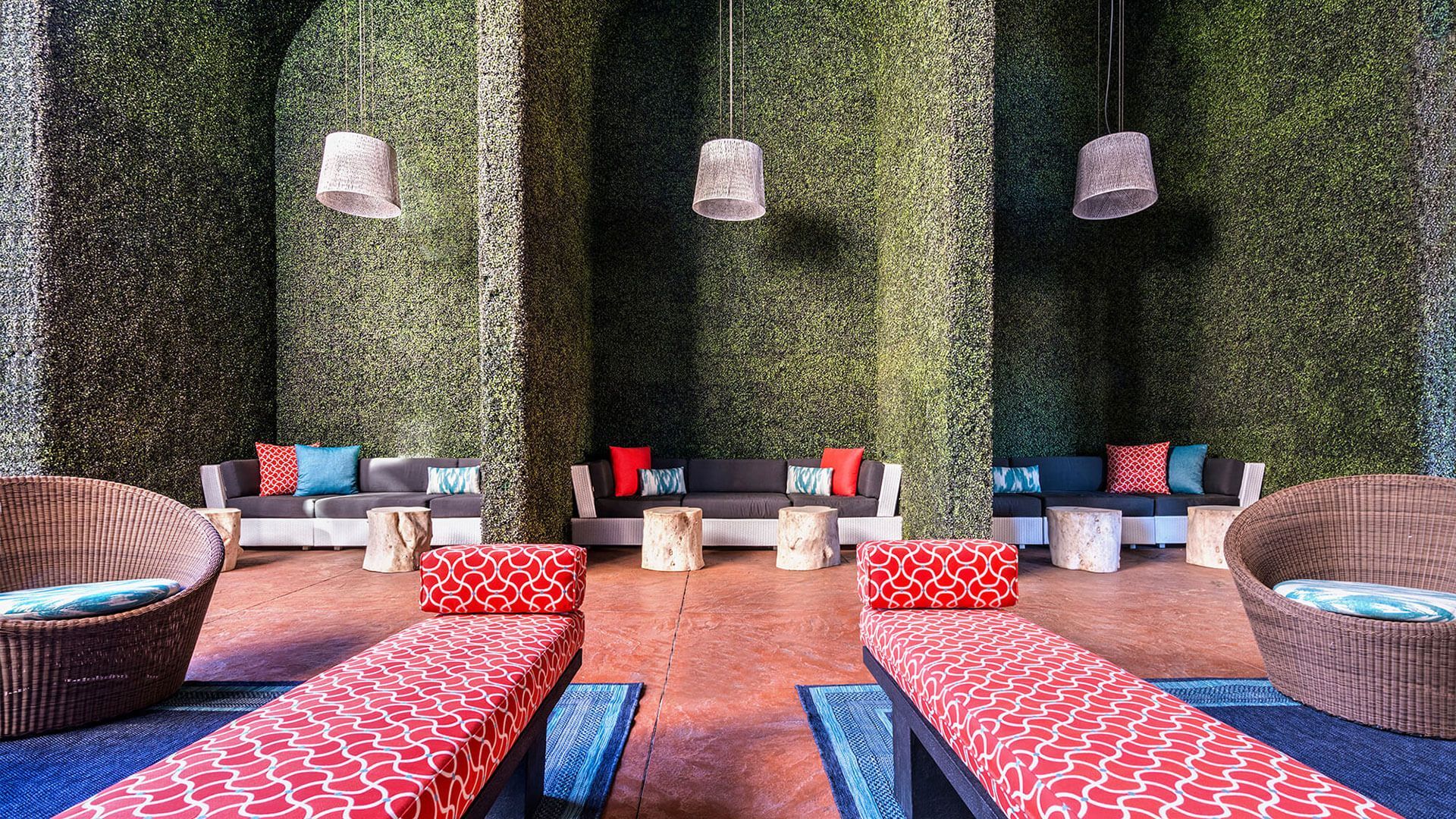 Lounge area with vertical garden walls, couches, and lounge chairs. Hanging lights and wood stools add to the decor.