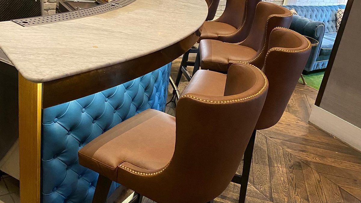 Brown bar stools at a blue, lit-up bar. The bar has a cream-colored top.