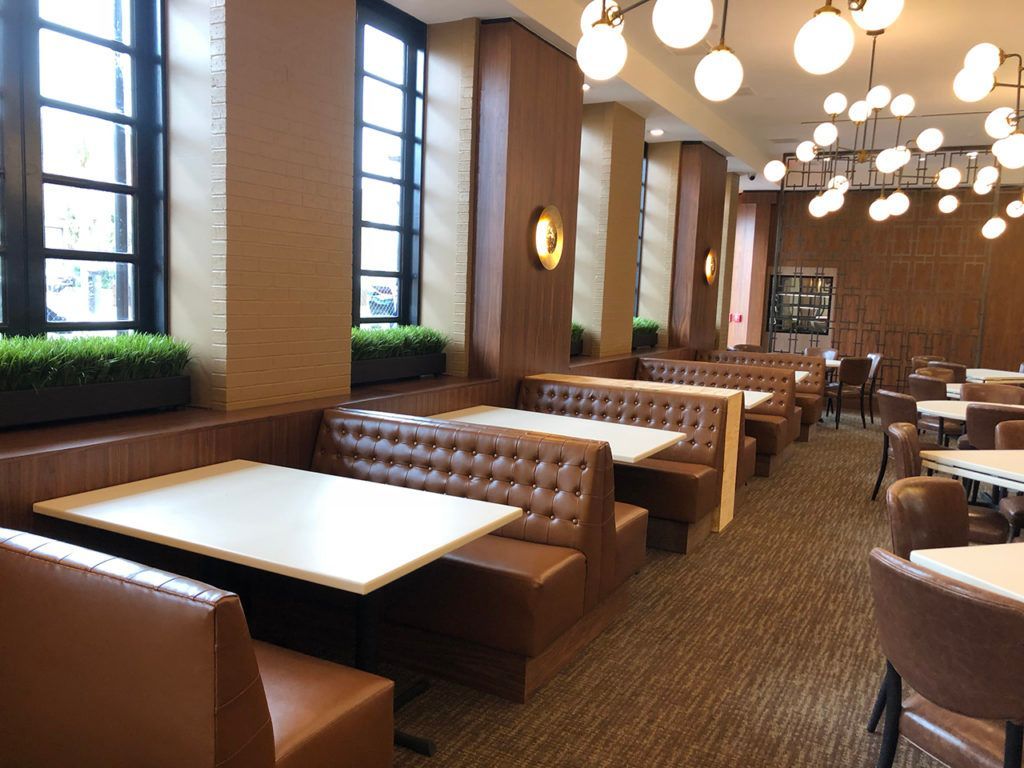 Restaurant booth seating with brown leather, white tables, and large windows.