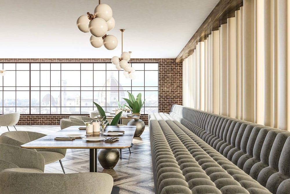 Upscale restaurant interior with long gray booth, tables, and large windows.