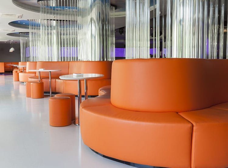 Orange curved sofas and round tables in modern interior with silver columns.