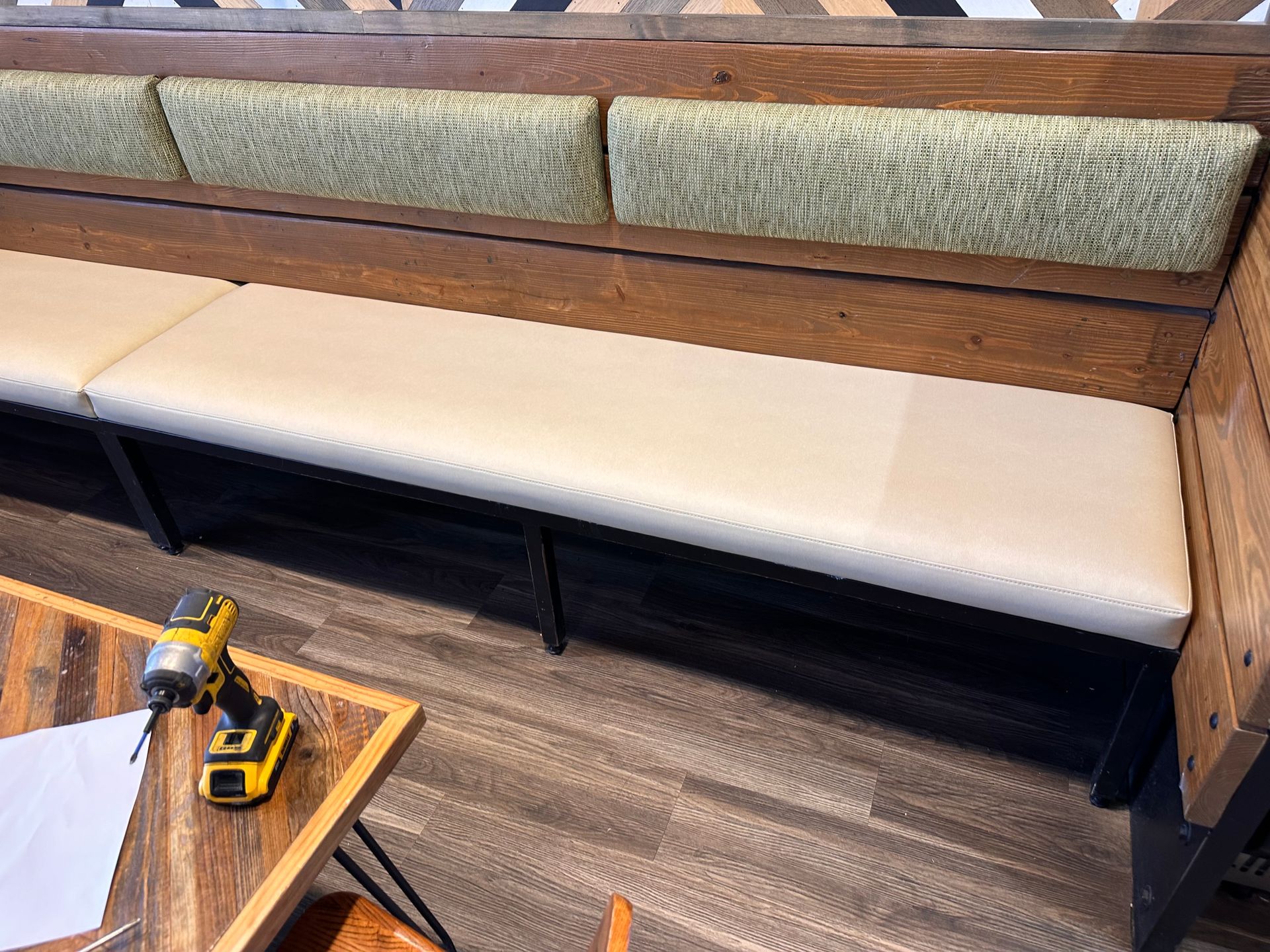 A bench with a white cushion is sitting next to a table with a drill on it.