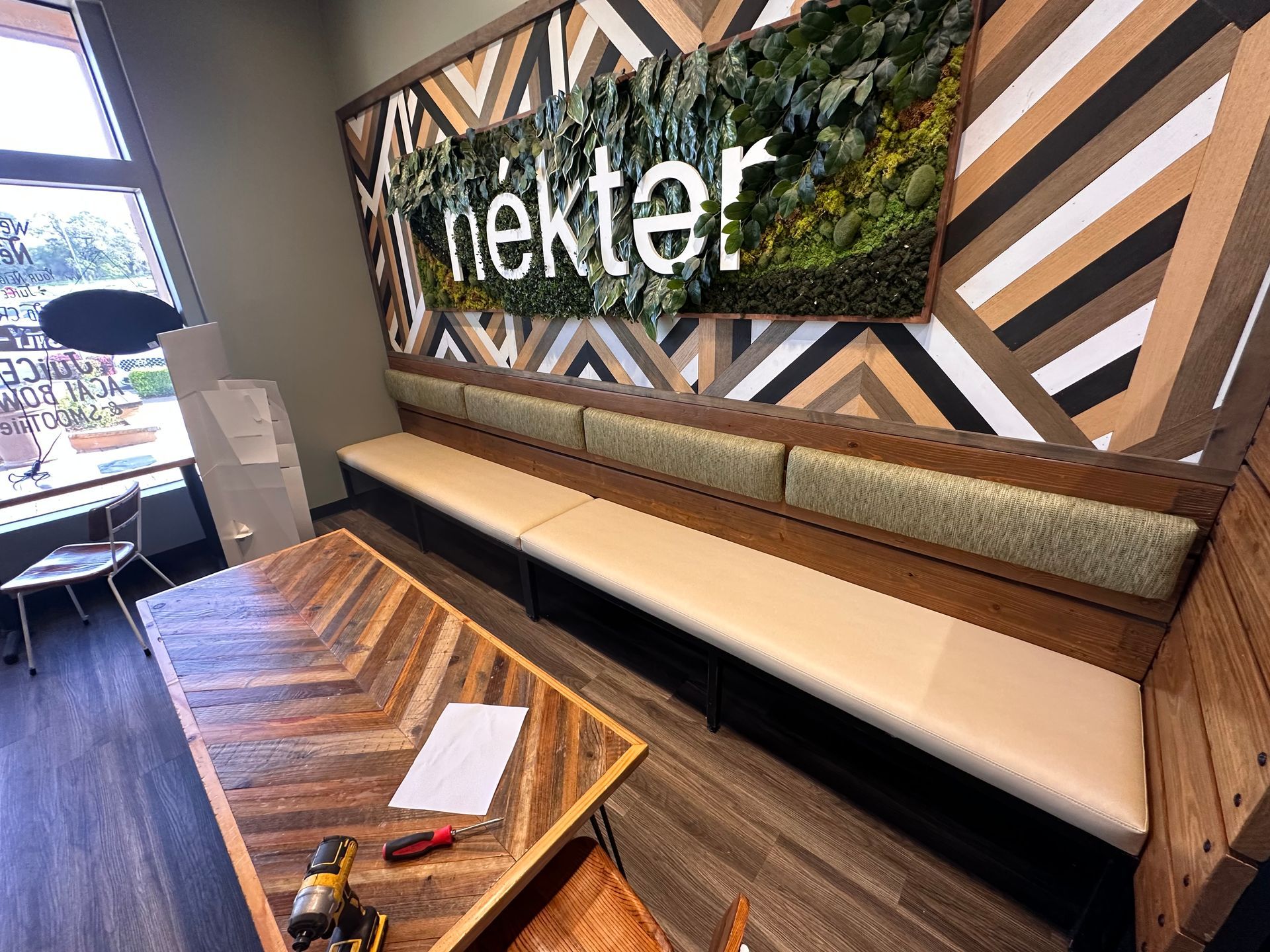 A waiting room with a wooden table and benches and a sign on the wall that says nektar.