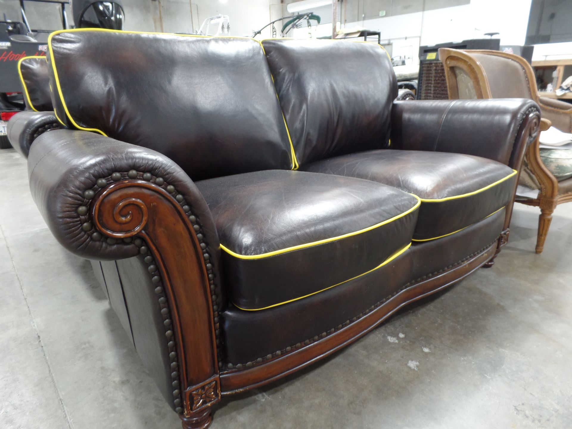 A brown leather couch with yellow trim sits in a warehouse