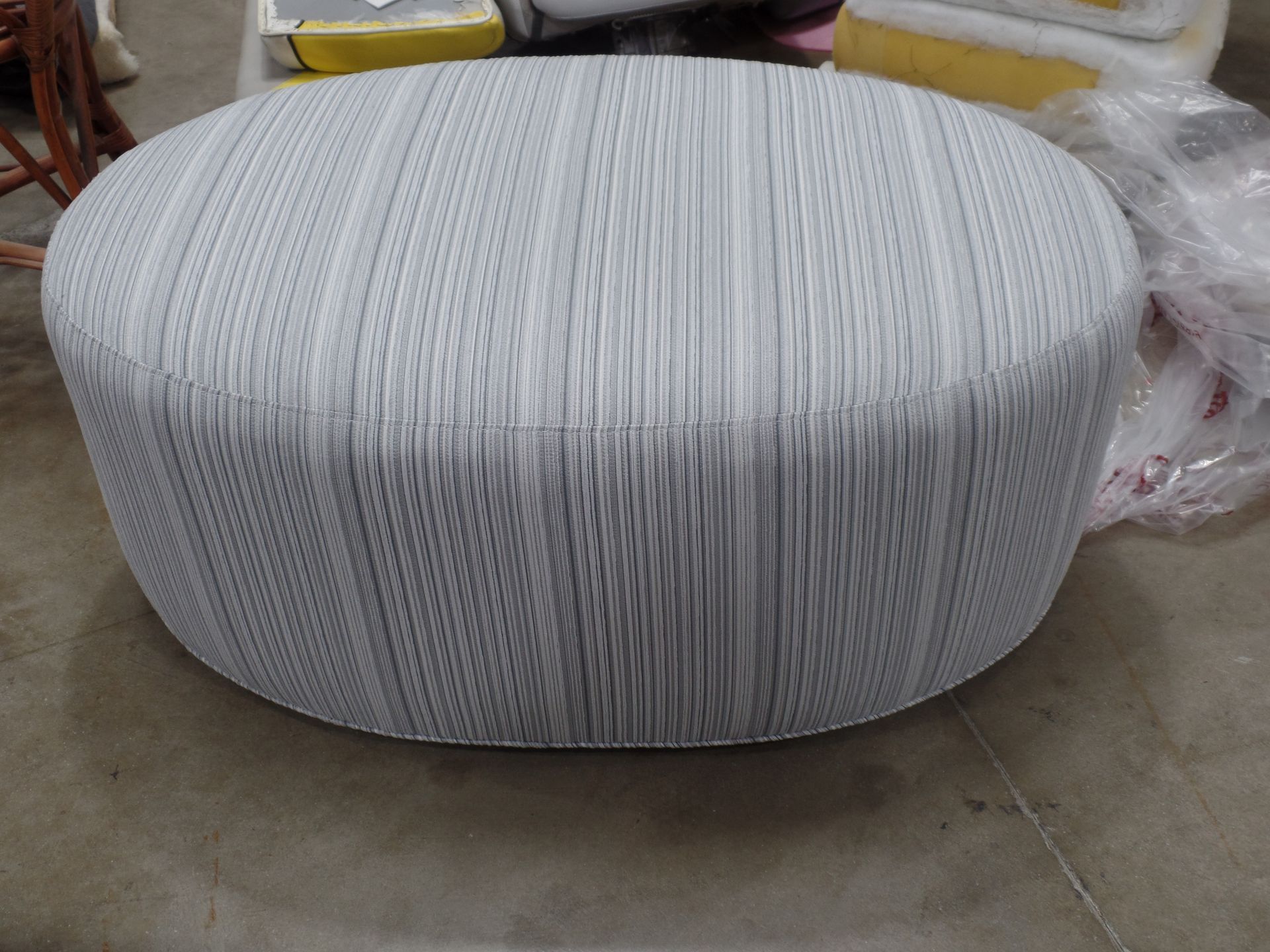 A white striped ottoman is sitting on a concrete floor.