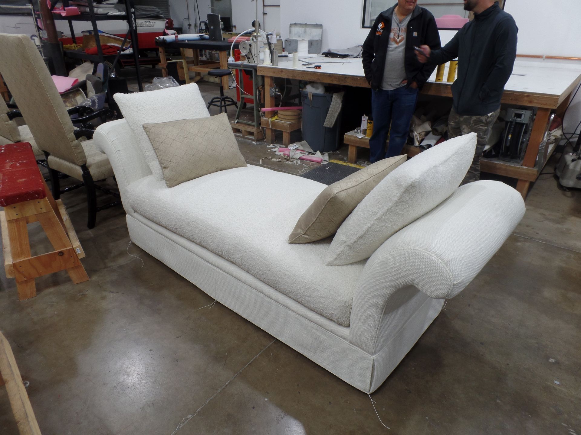 Two men are standing next to a white chaise lounge in a room.