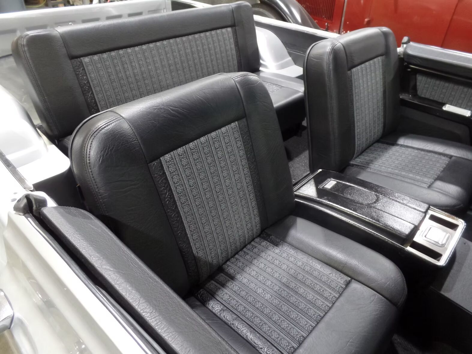 The interior of a car with black and grey seats and a red car in the background.