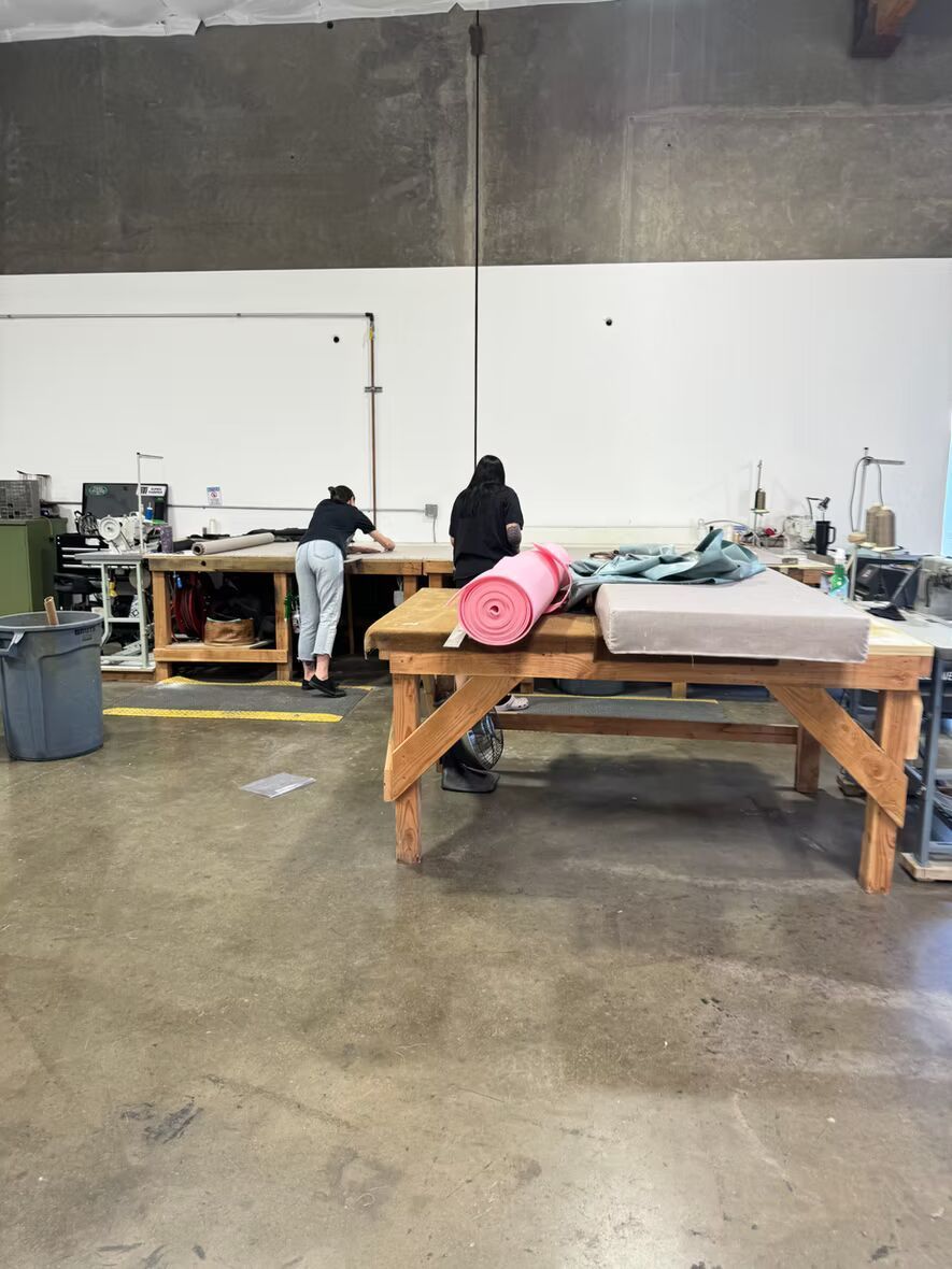 A woman is sitting at a wooden table in a factory.