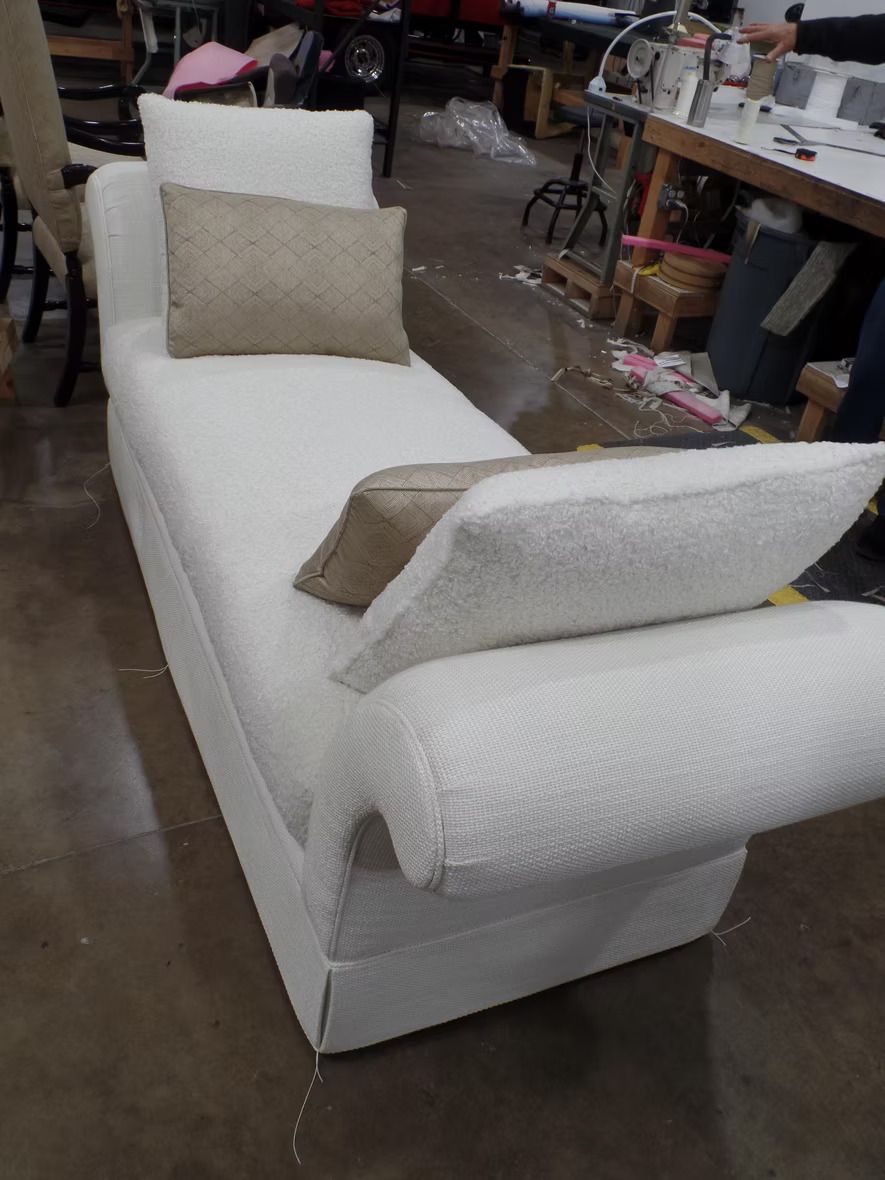 A white chaise lounge with two pillows on it is sitting in a room.