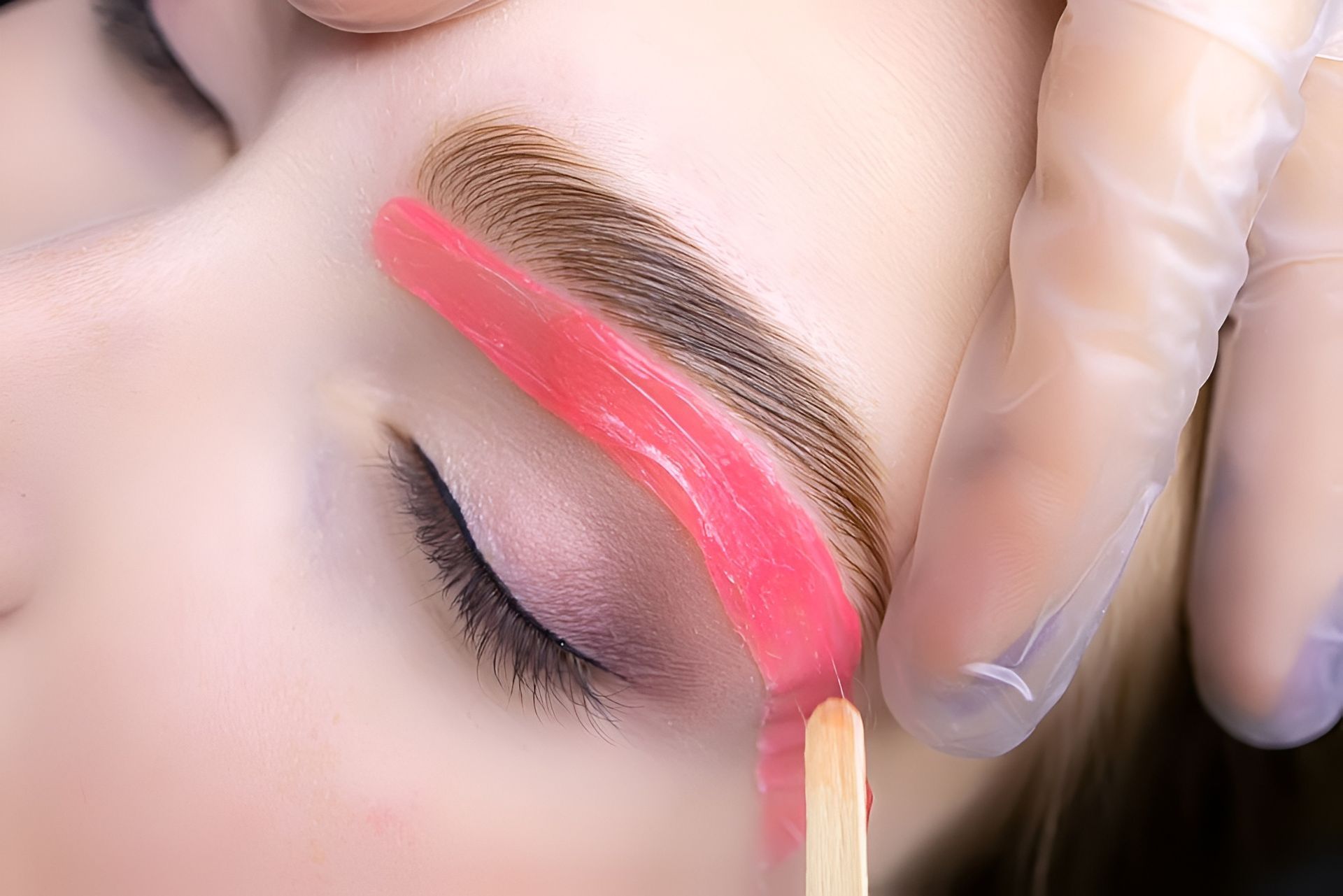 Wax being applied to eyebrow; close-up view of a beauty treatment. Pink wax on skin, gloved hand. Admire Skincare and Beauty in Taree, NSW