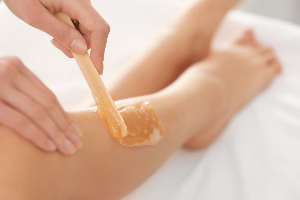 A person waxing a leg with a wooden applicator, on a white surface. — Admire Skincare and Beauty in Taree, NSW