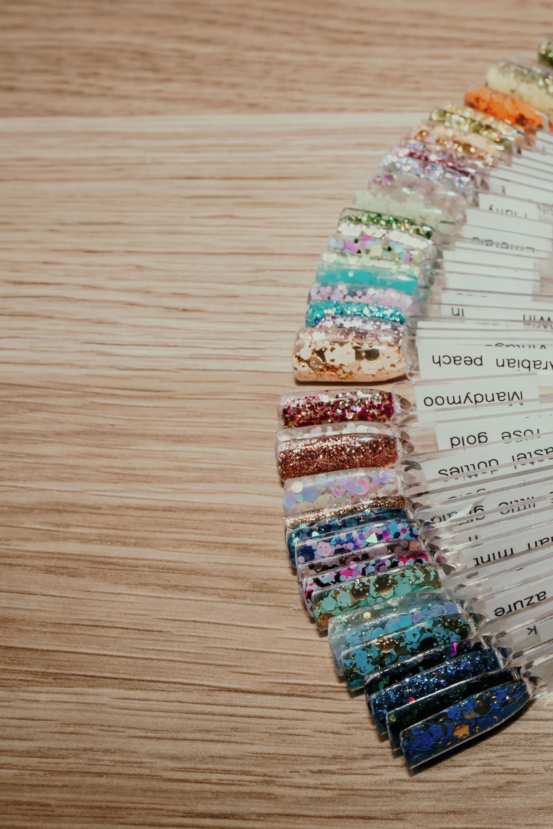 Nail polish colour swatches in various glittery shades arranged on a wooden surface.  — Admire Skincare and Beauty in Taree, NSW