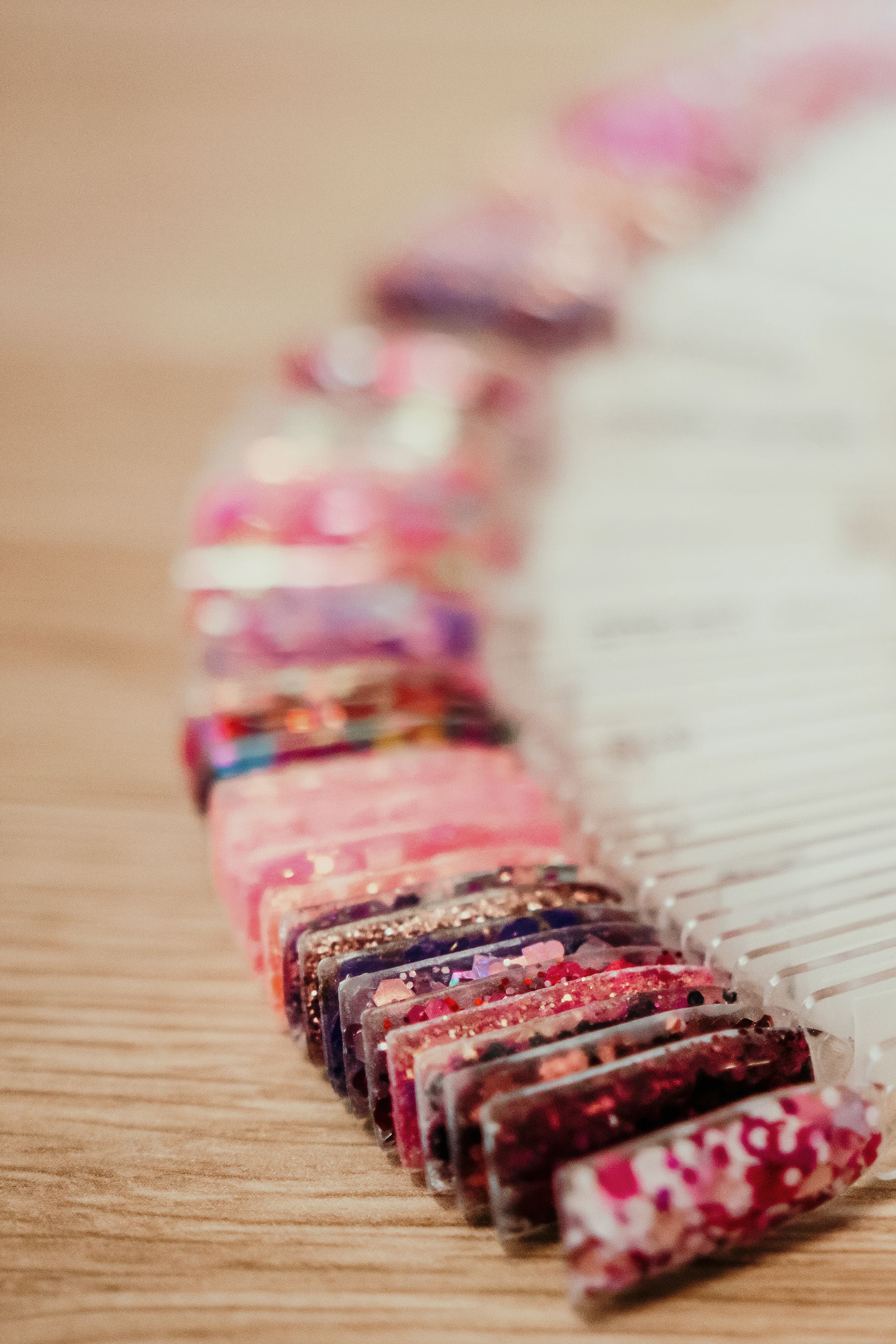 Close-up of a fan of painted nail swatches on a wooden surface, with a range of pink, purple, and glitter designs. — Admire Skincare and Beauty in Taree, NSW